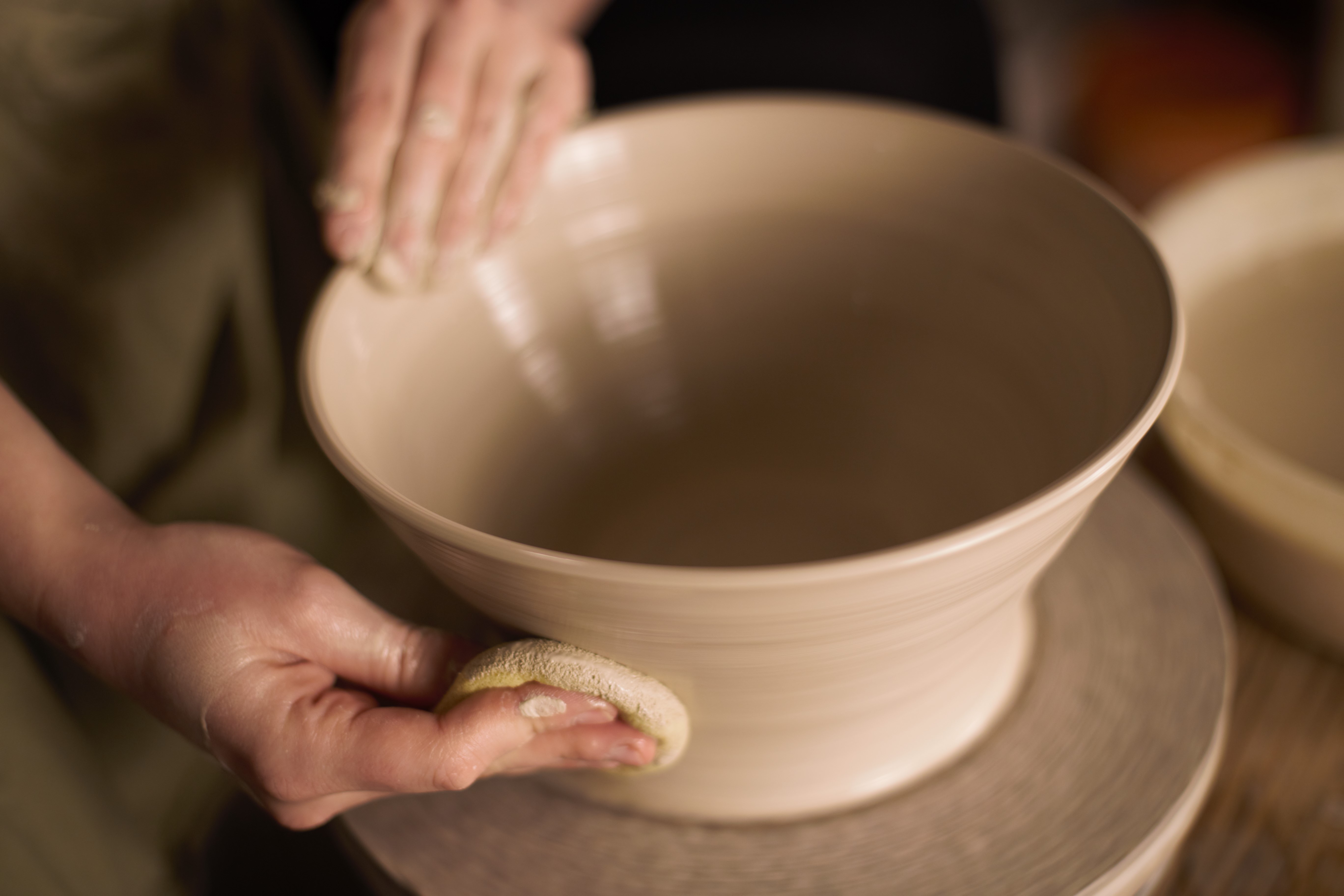 Hands shaping a clay bowl on wheel.
