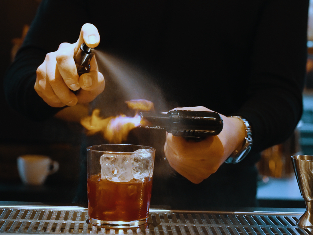 Bartender igniting cocktail with spray and flame.