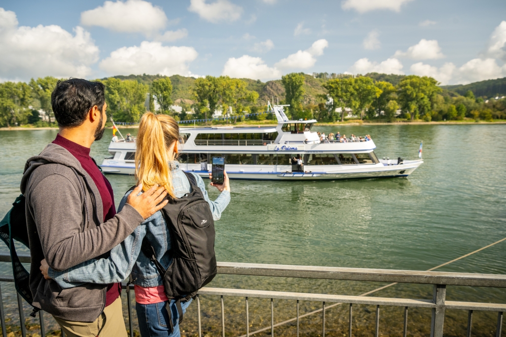 Paar beobachtet Boot auf Fluss, malerischer Hintergrund.