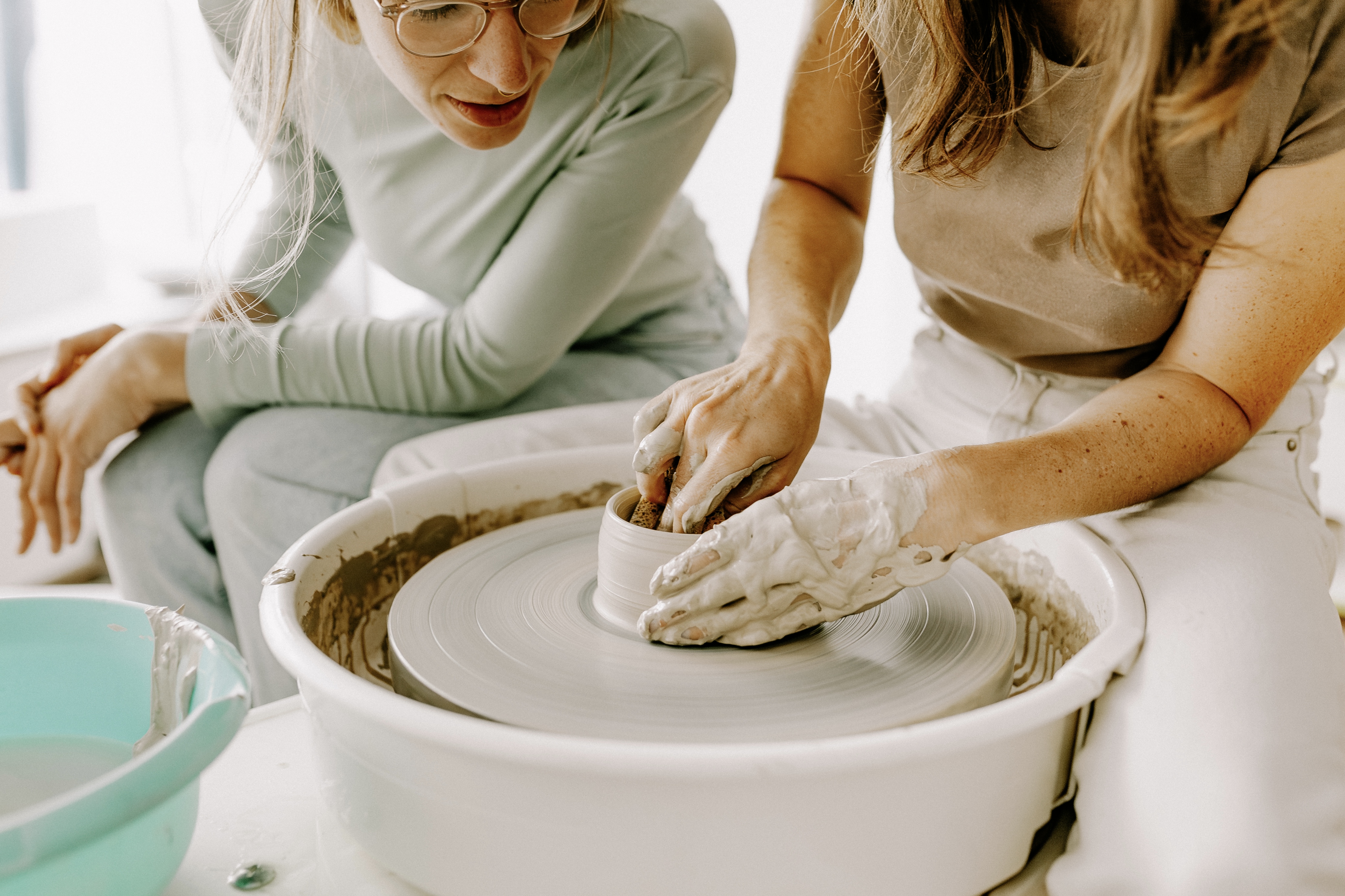 Two women crafting pottery on wheel indoors.