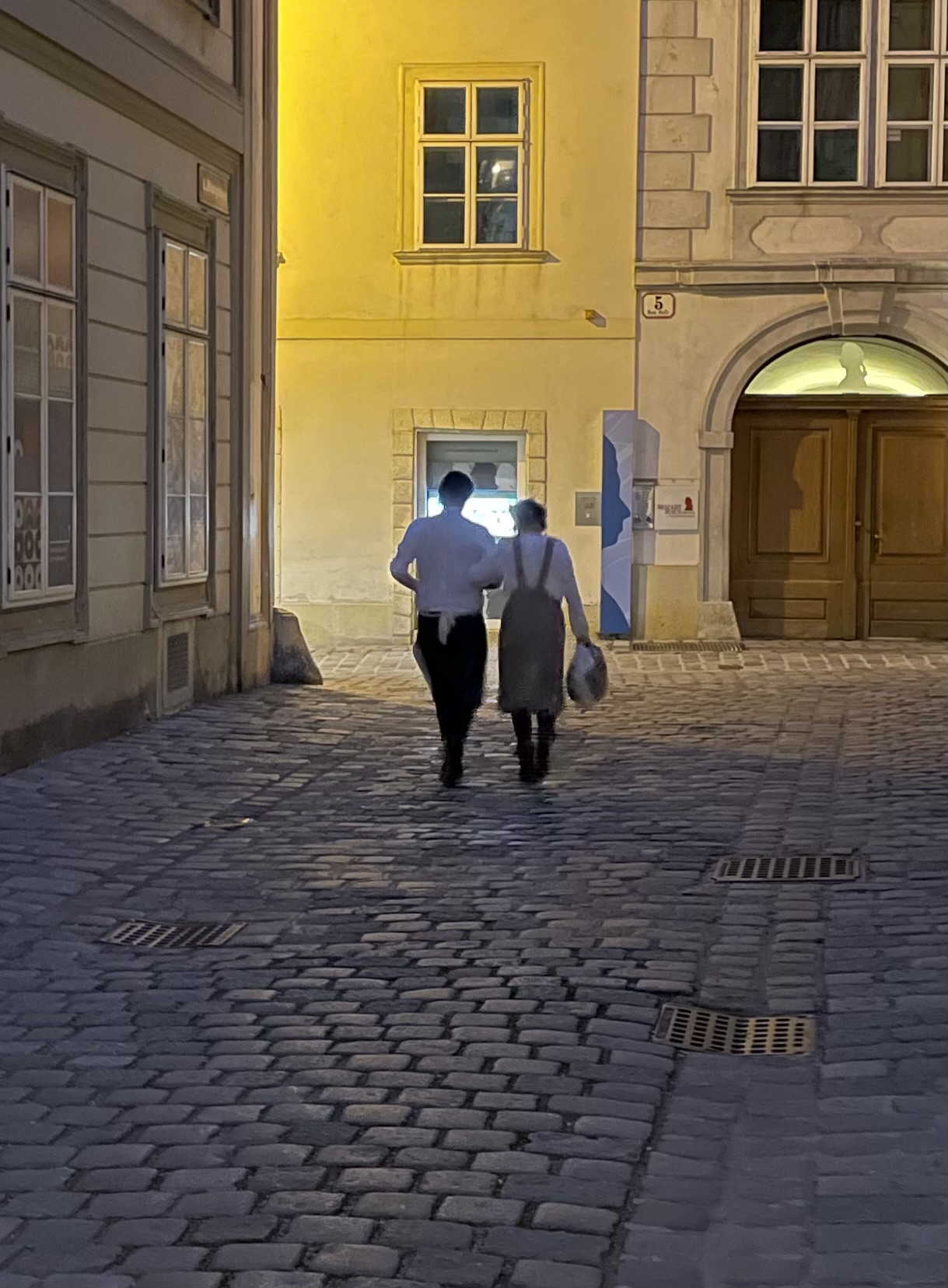 Two people walking in dimly lit street.
