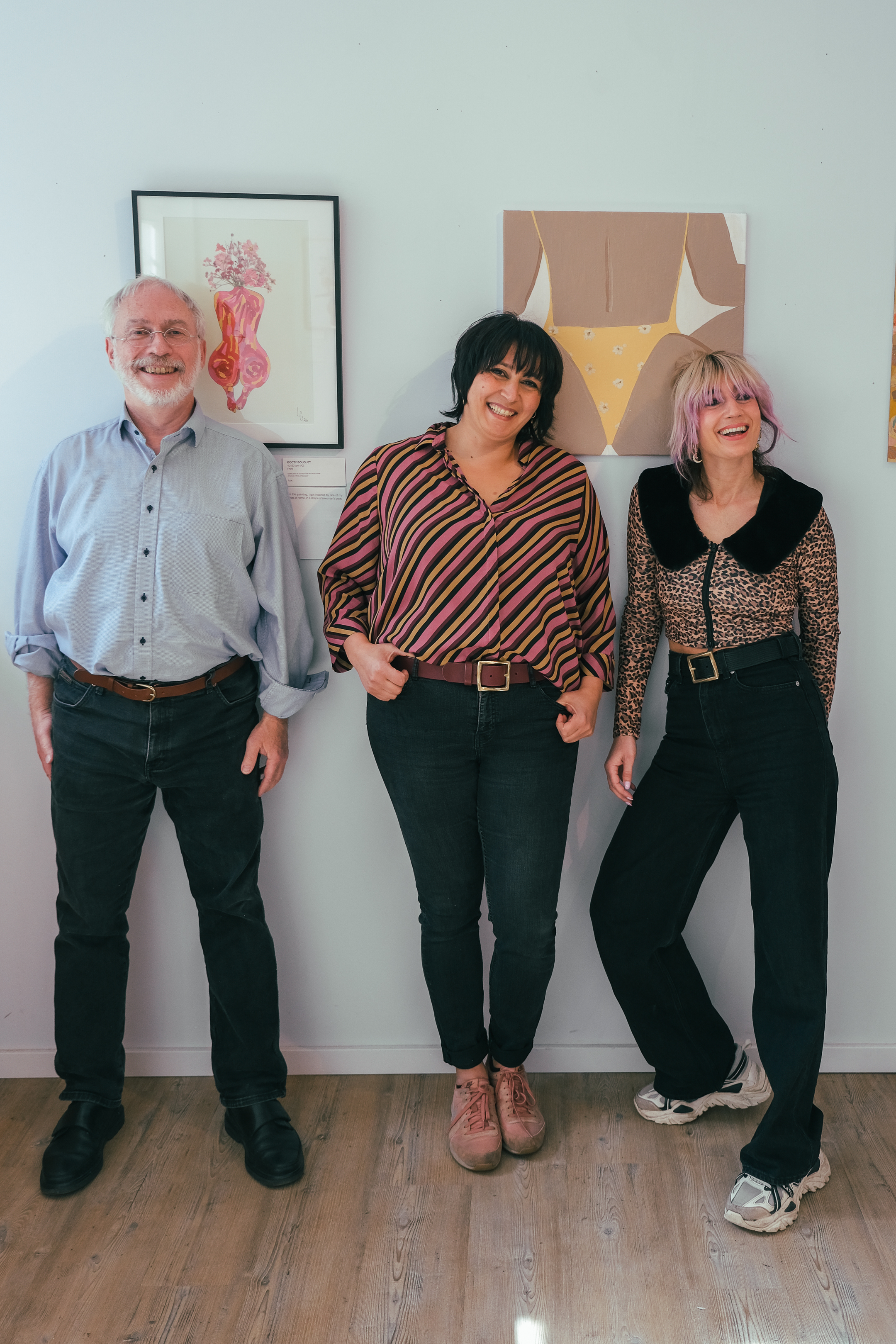 Three people smile together in front of colorful works of art.