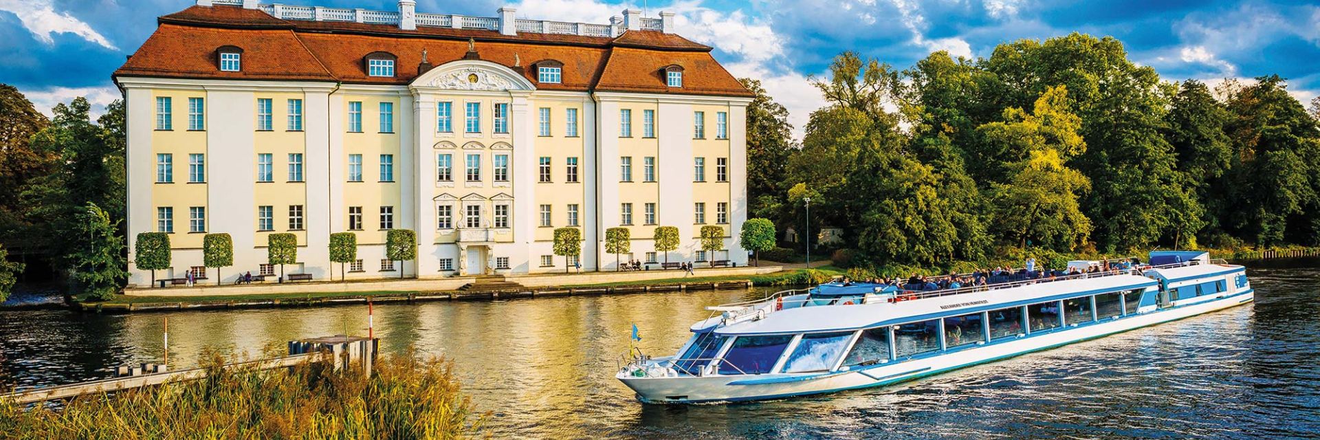 Boat cruising past historic building and trees.