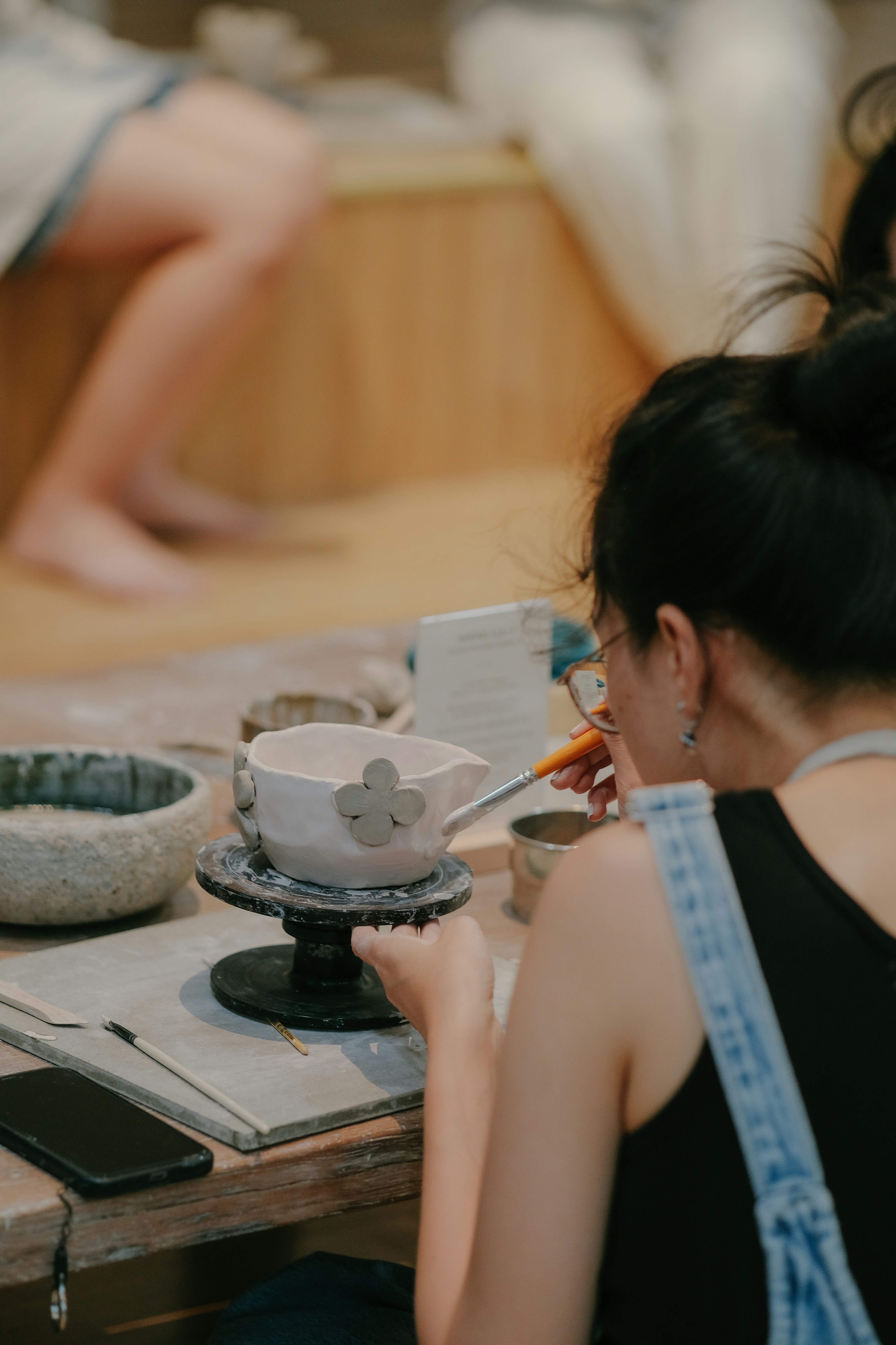 Person painting clay bowl with flowers indoors.