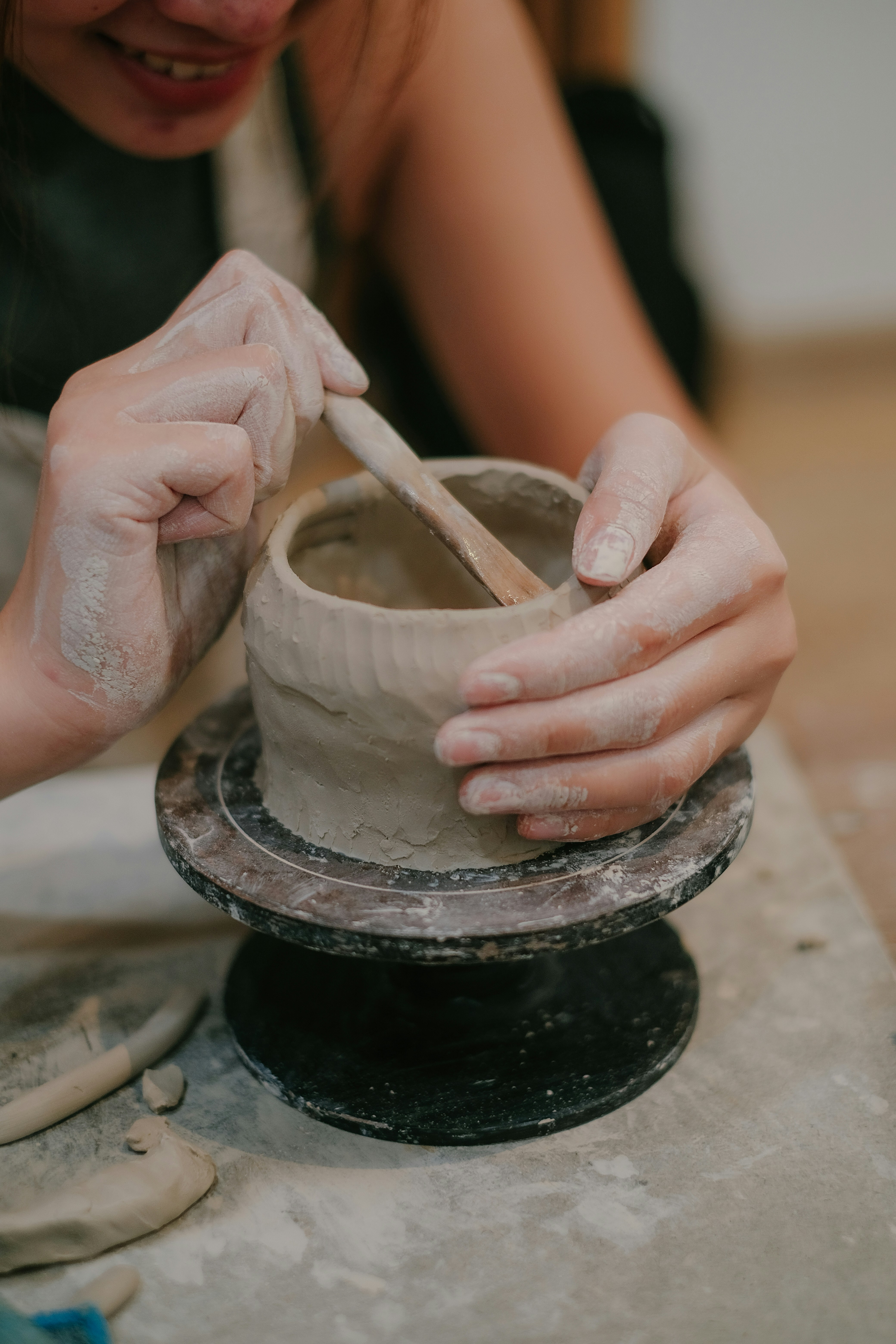 Hands sculpting clay pot on a wheel.