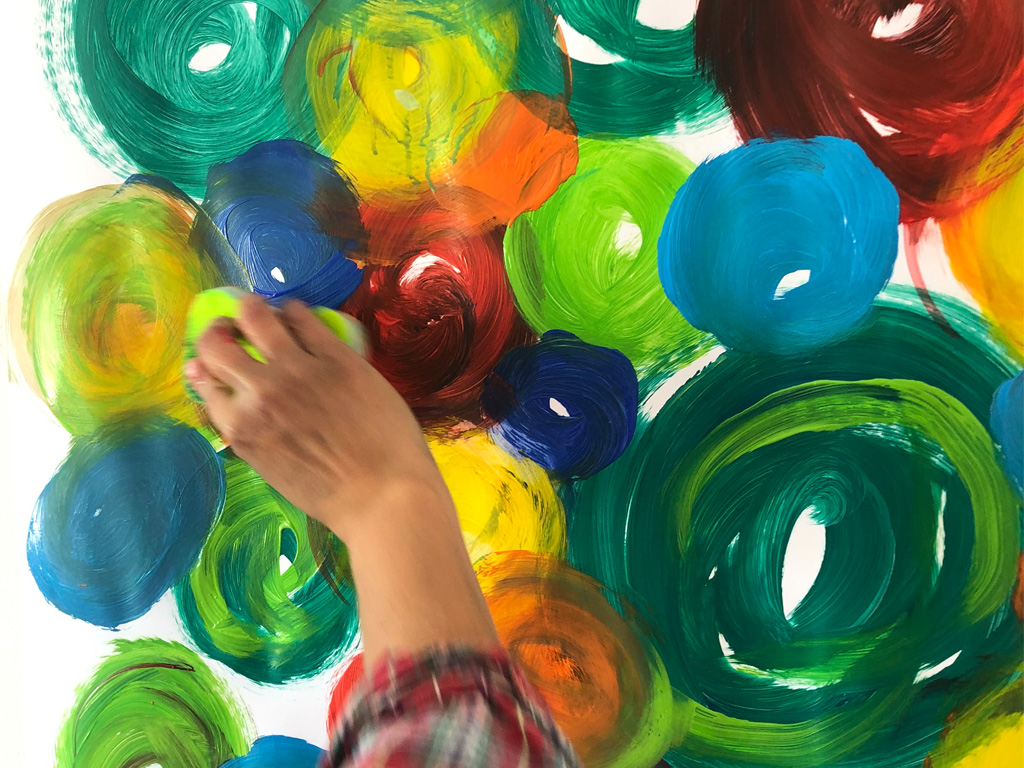 Hand painting colorful spirals on white surface.