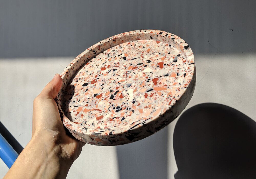Hand hält Terrazzo-Tablett im Sonnenlicht.