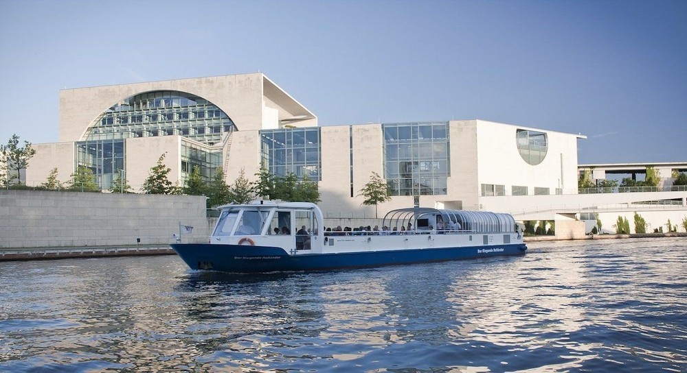 Touristenboot passiert Regierungsgebäude am Fluss.