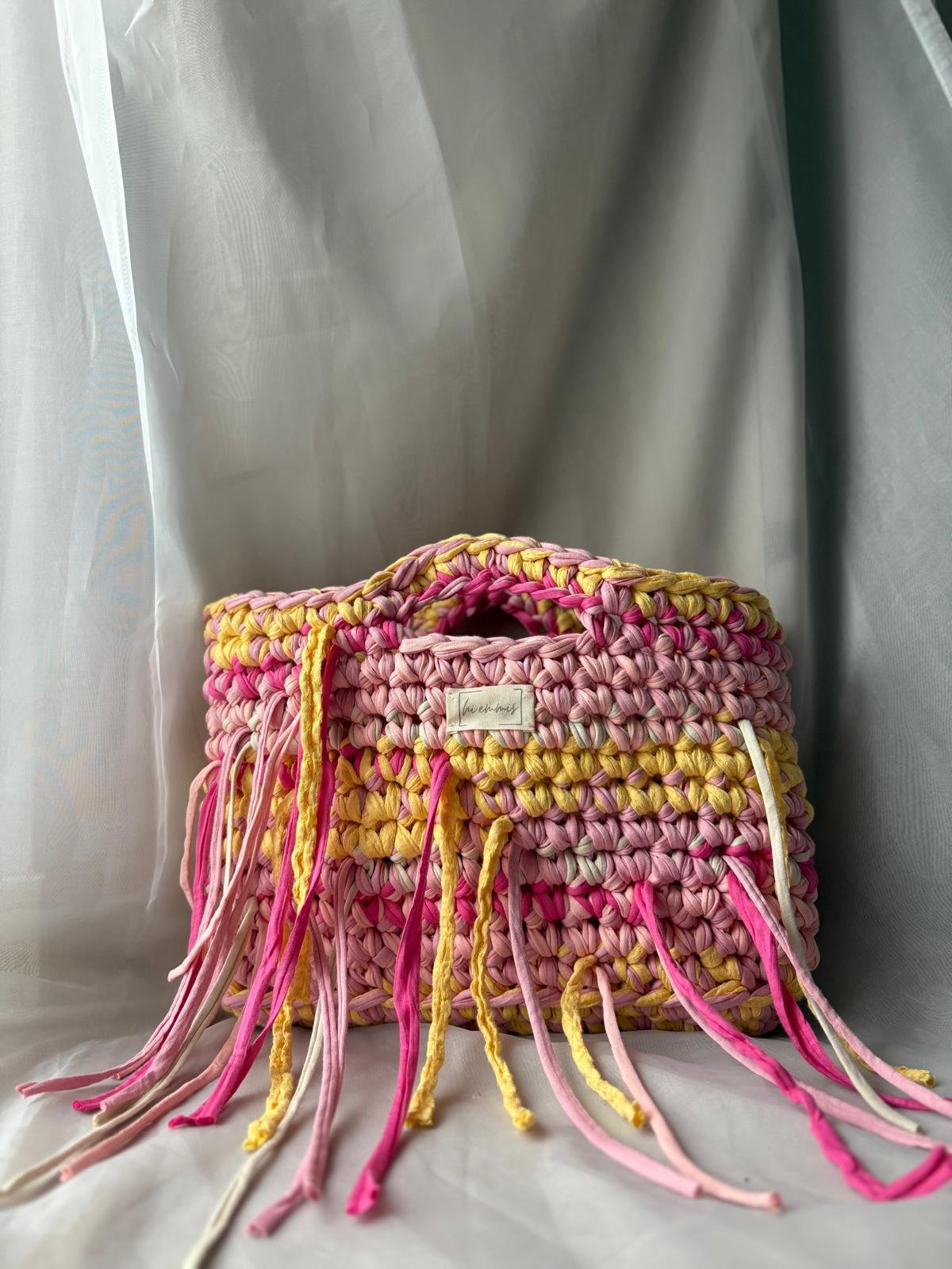 Bunte gehäkelte Tasche mit Fransen im Raum.