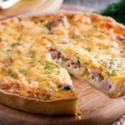 Quiche slice being served on wooden board.