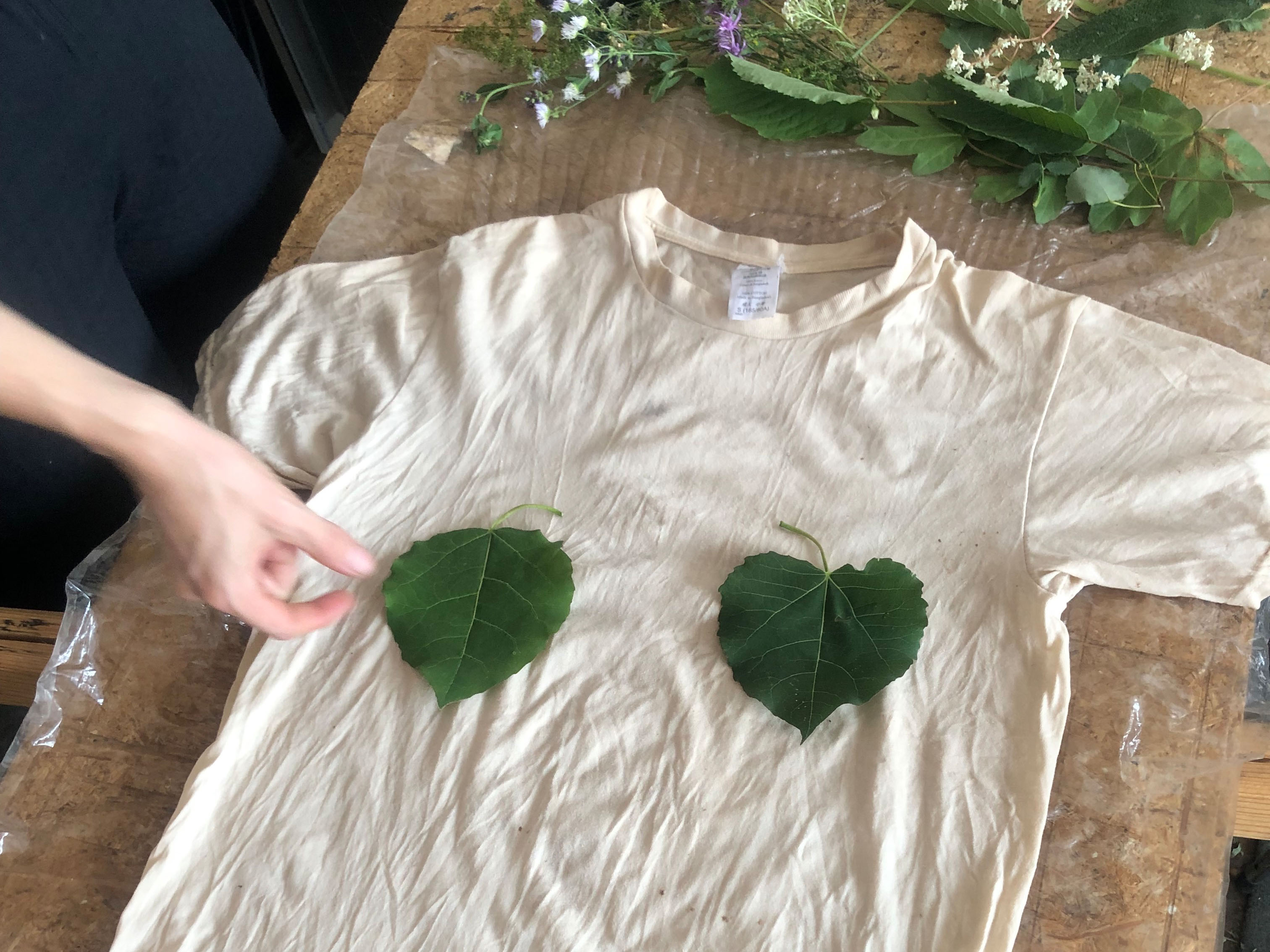 Hand legt Blätter auf ein weißes T-Shirt.
