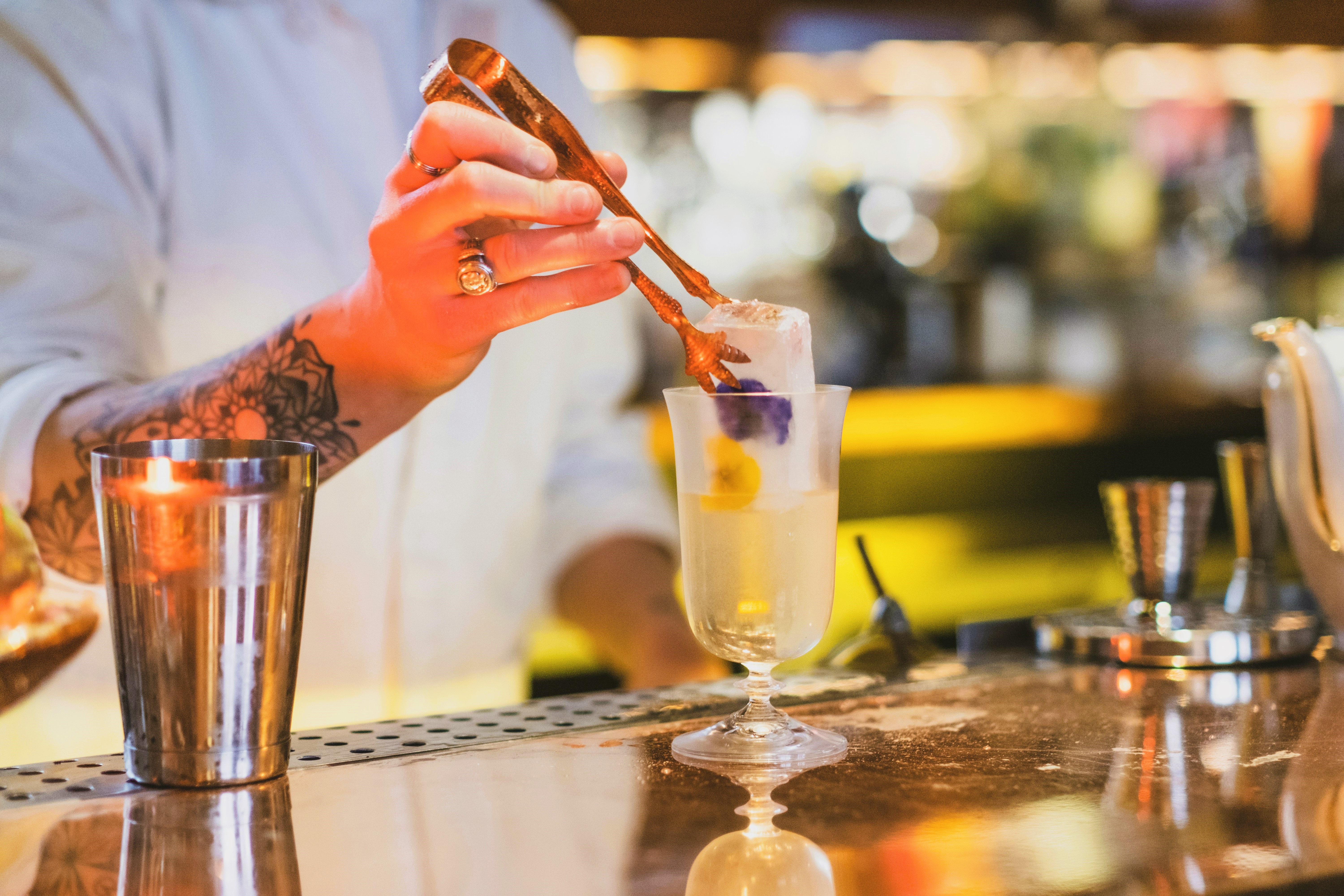 Barkeeper legt Eis in Cocktailglas an der Bar.