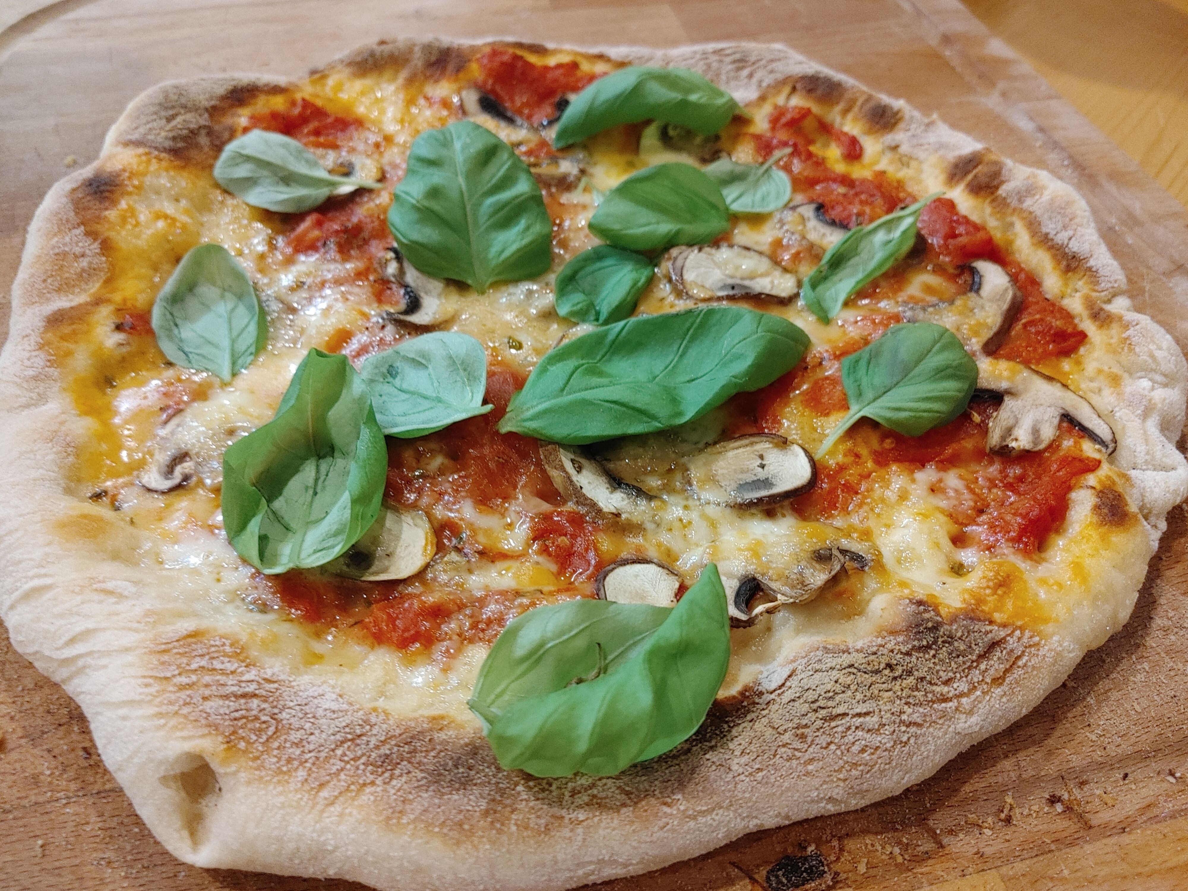 Pizza mit Basilikum und Champignons auf Holzbrett.