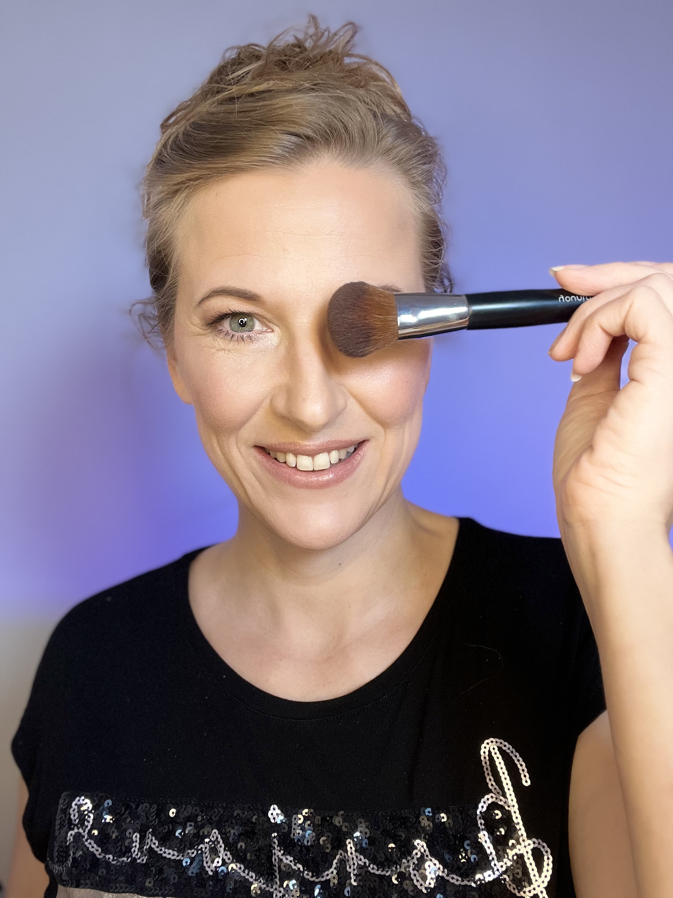 Woman holding makeup brush near her face.