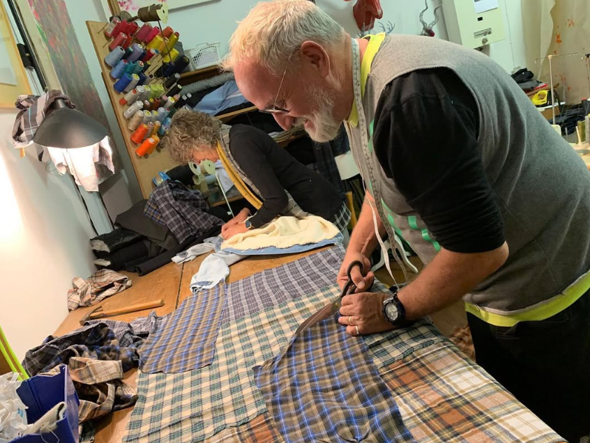 Two tailors cutting plaid fabric on a table.