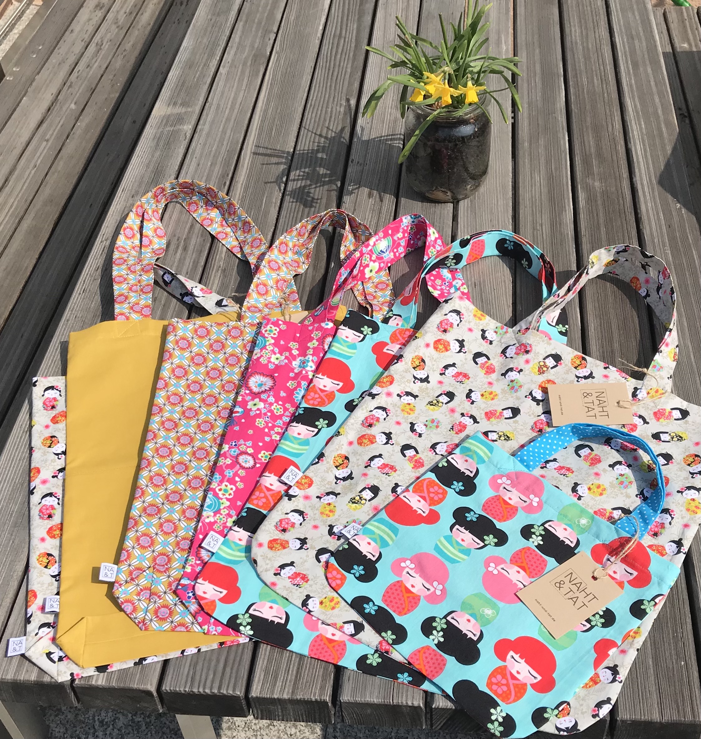 Colorful tote bags on wooden bench, bright designs.