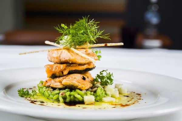 Grilled salmon piled on green risotto, decorated with herbs.