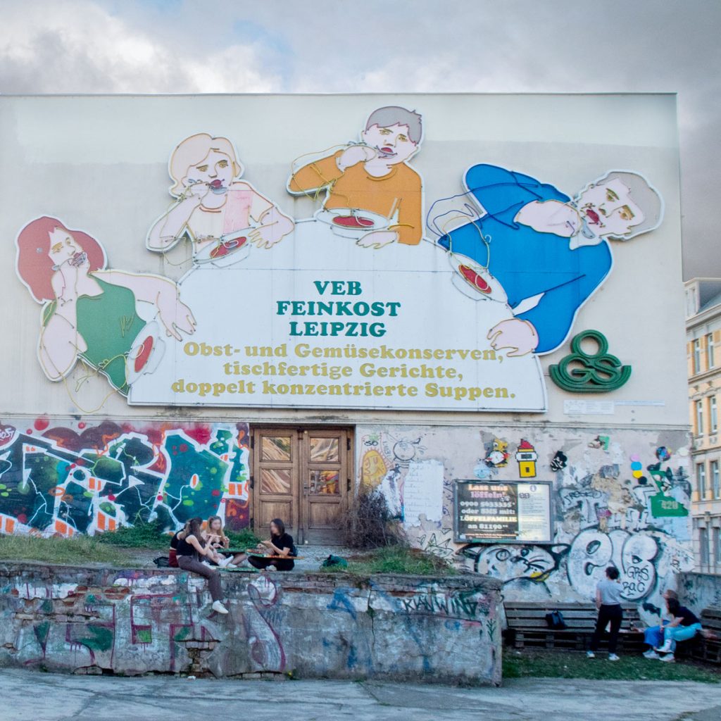 Four cartoon people eating soup on graffiti wall.