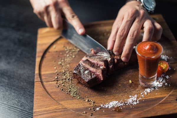 A steak is cut on a wooden board, with sauce.