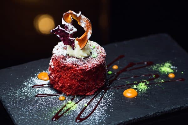 Red cake with cream, decorated on a black plate.