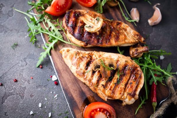 Gegrilltes Hähnchenfilet liegt mit Gemüse auf einem Holzbrett.