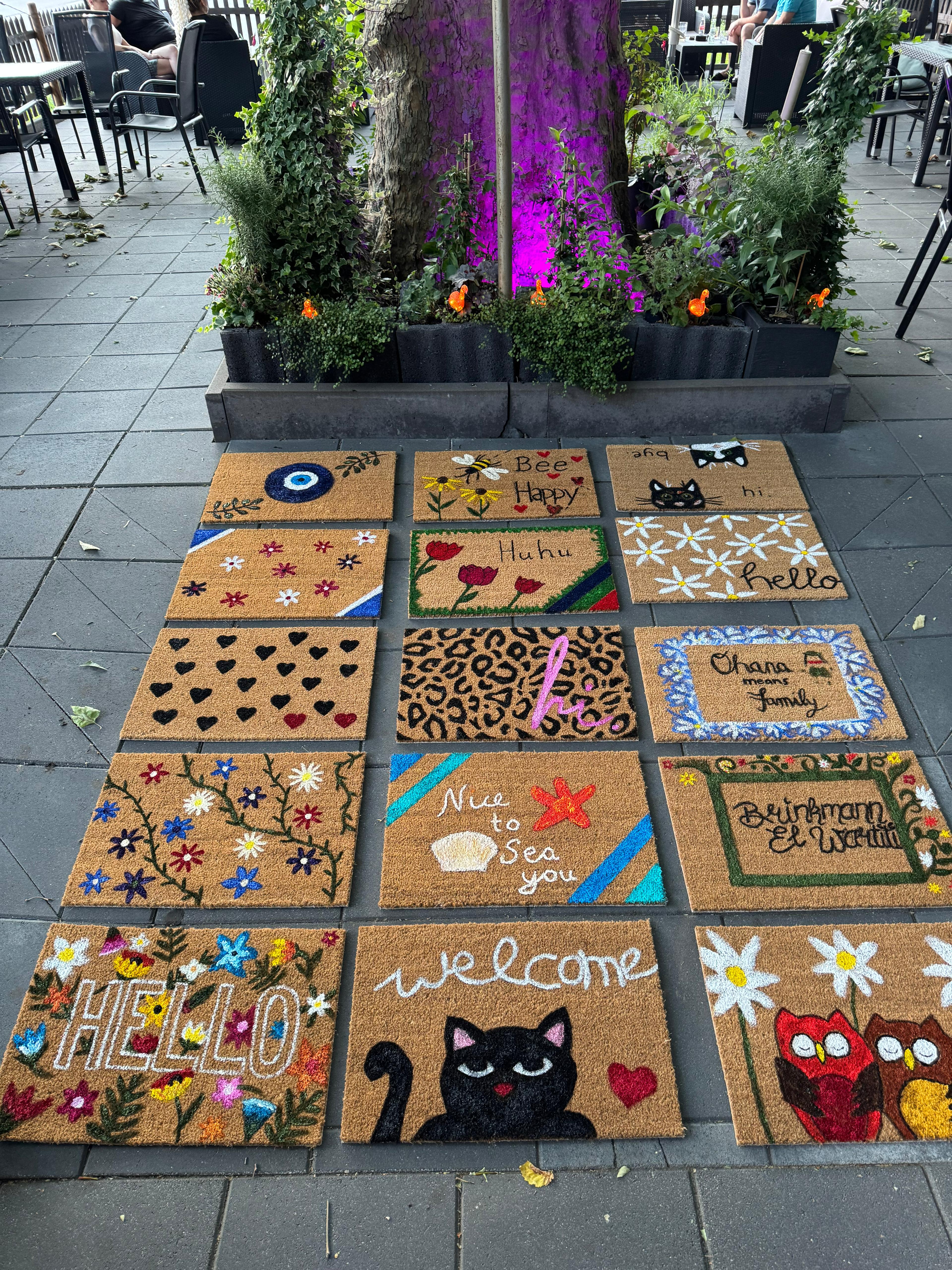 Colorful doormats displayed on a sidewalk.