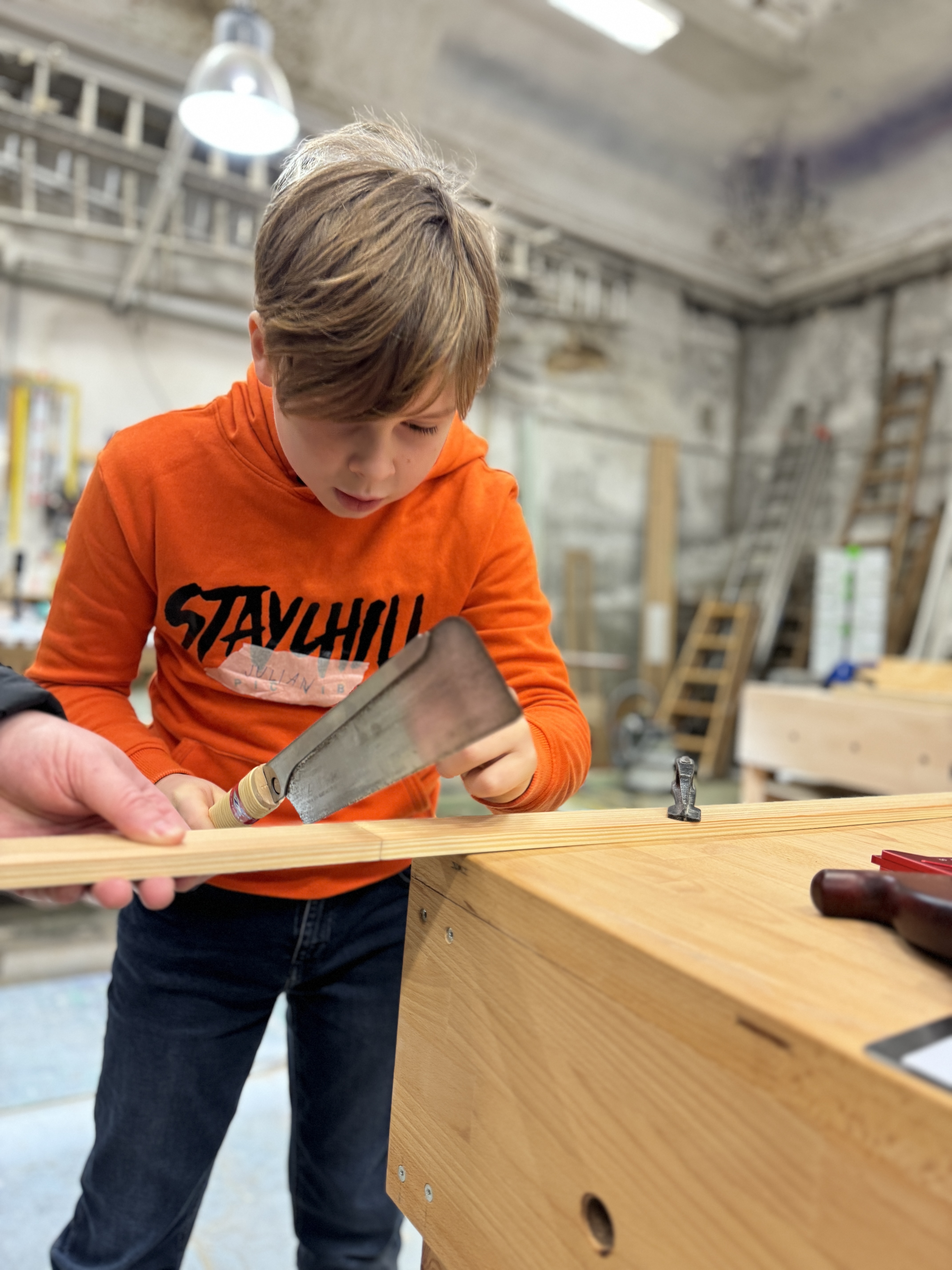Kind sägt Holz in einer Werkstatt.