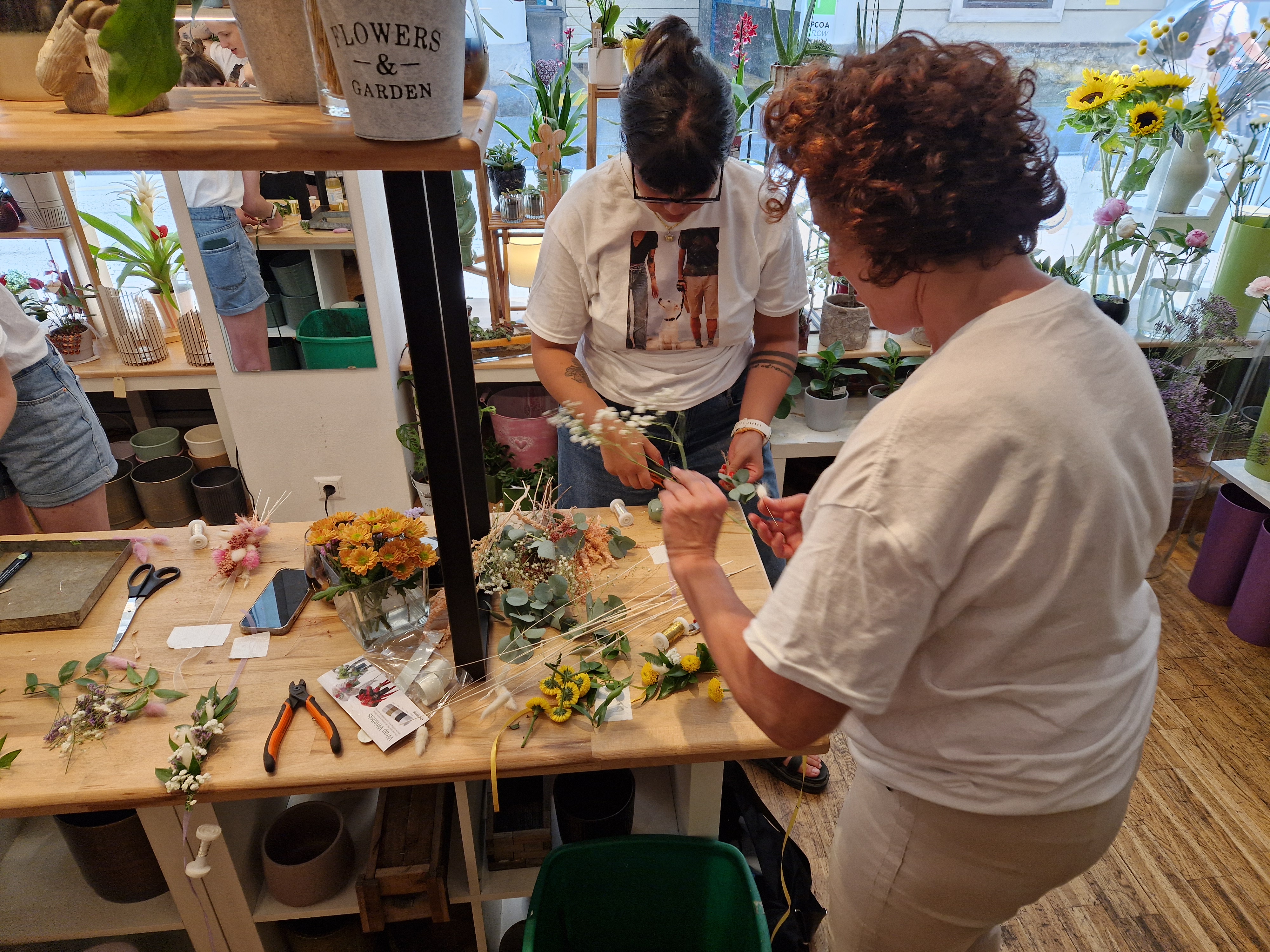 People arranging flowers on a wooden table.