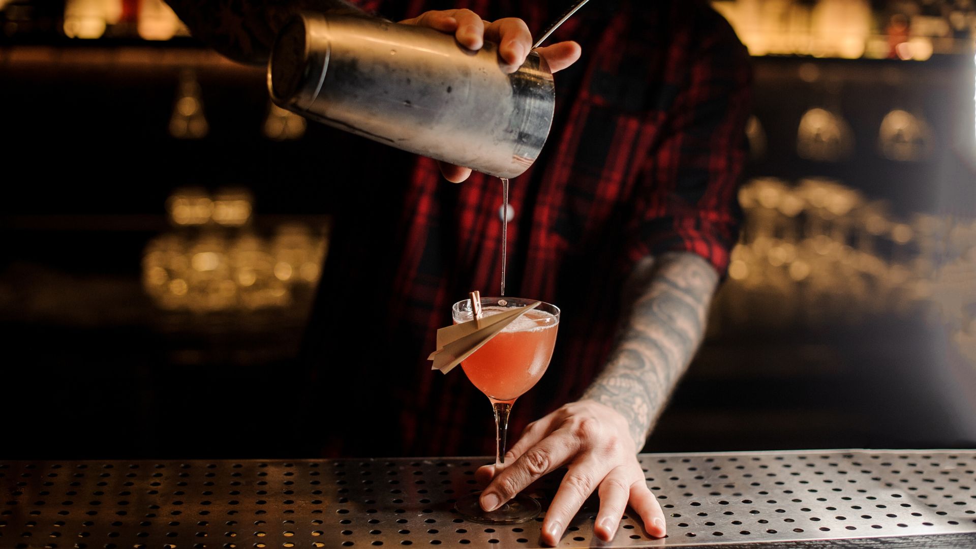 Bartender pouring cocktail at dimly-lit bar.