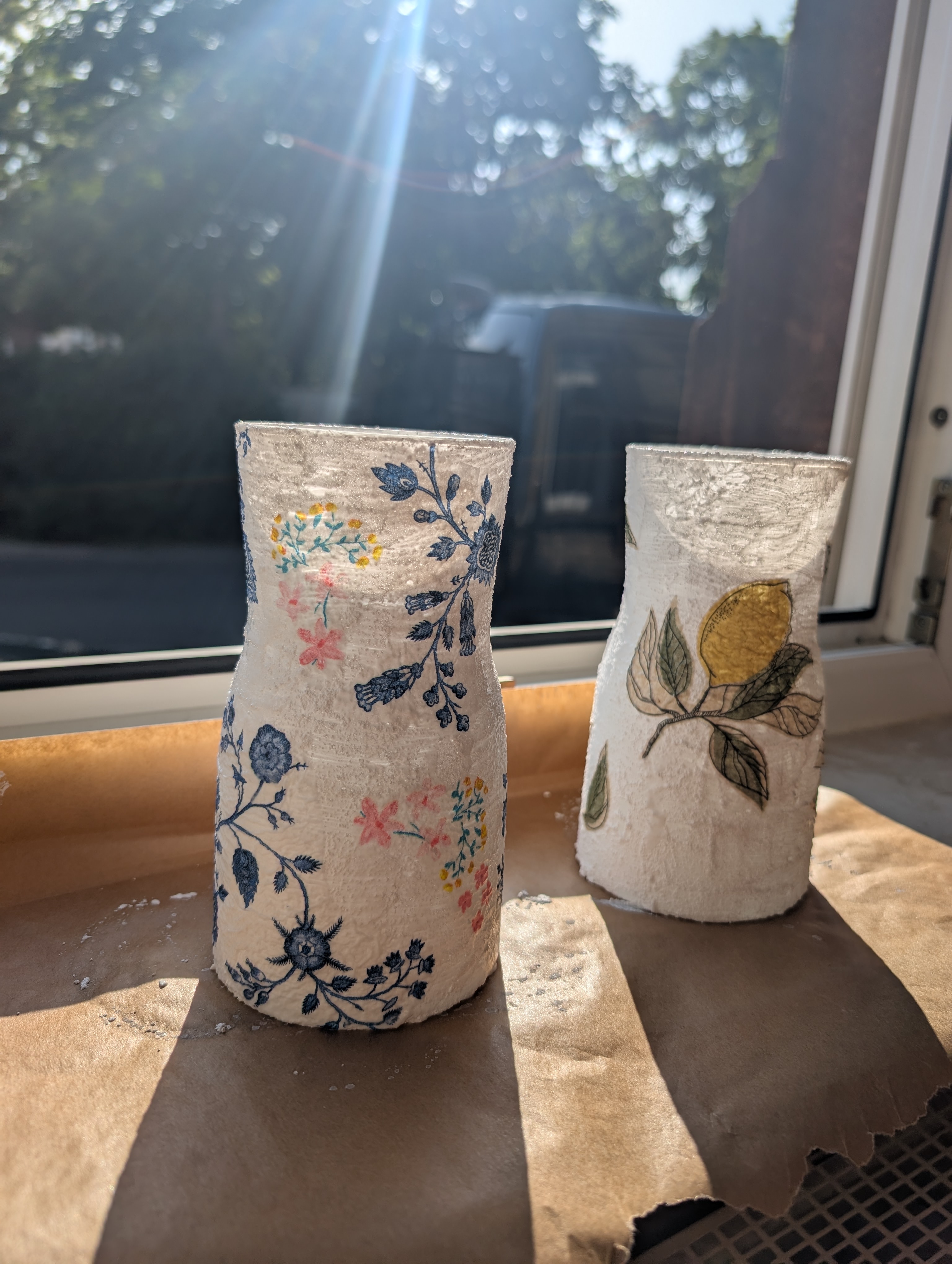 Two decorative vases with floral designs on windowsill.