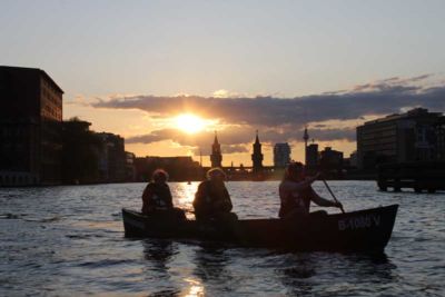 Personen paddeln auf Fluss bei Sonnenuntergang.