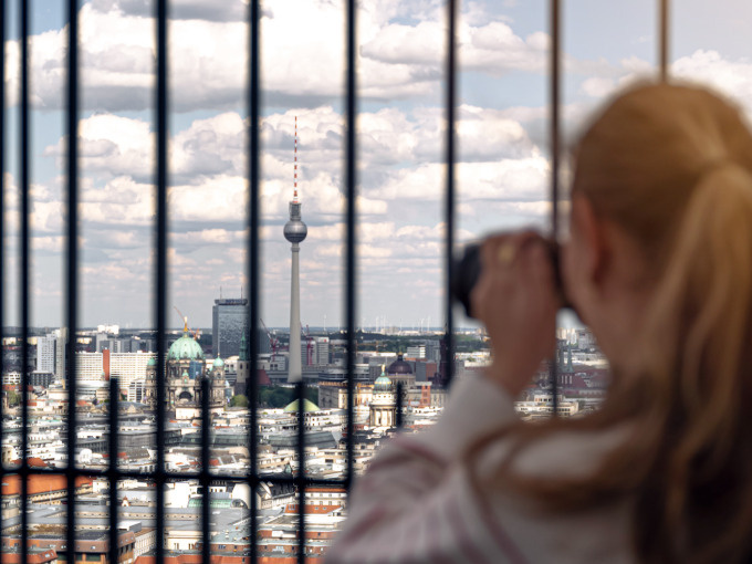 Person fotografiert Berliner Skyline durch Gitterstäbe.