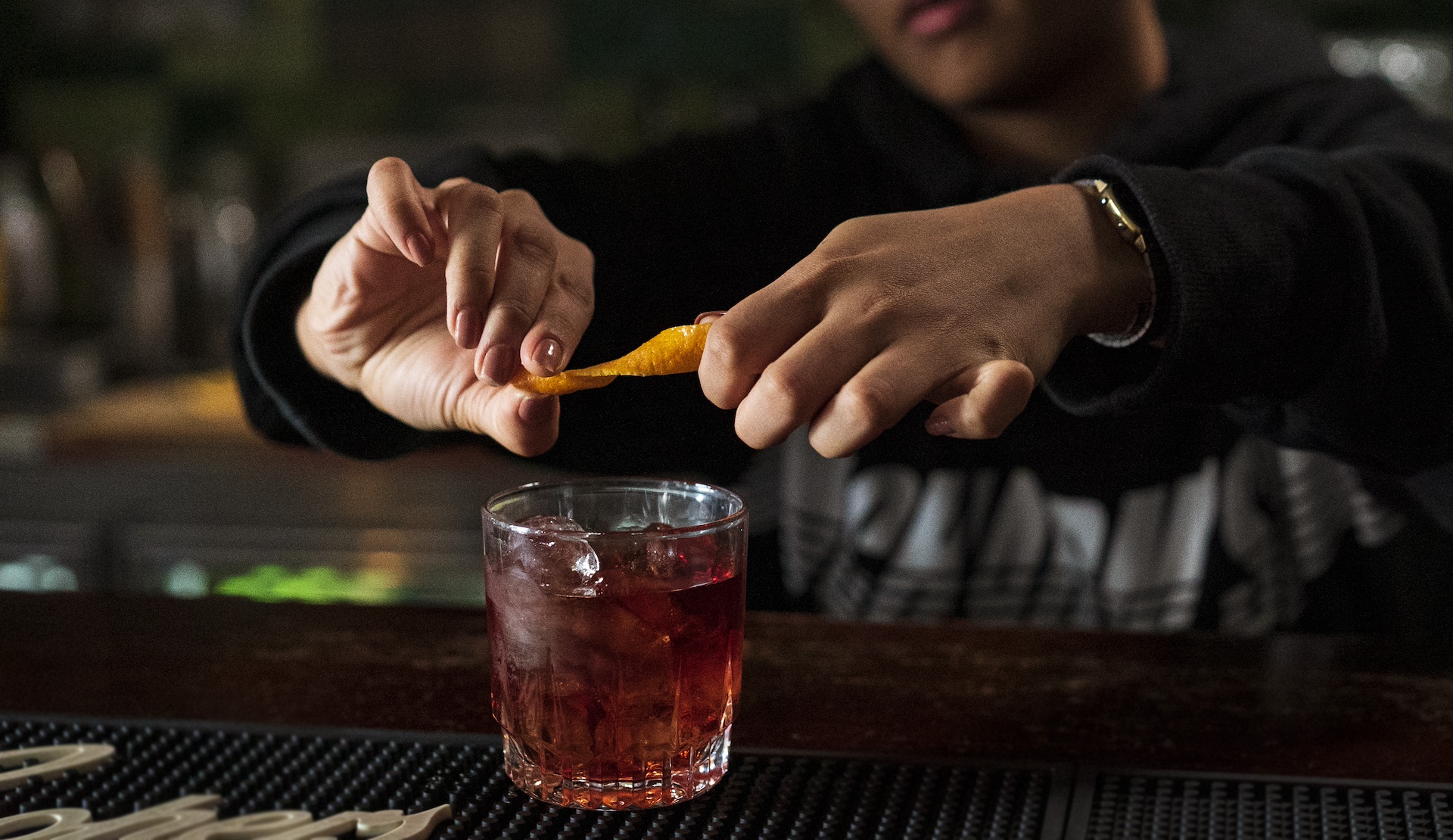 Barkeeper garniert Cocktail mit Orangenschale an Bar.