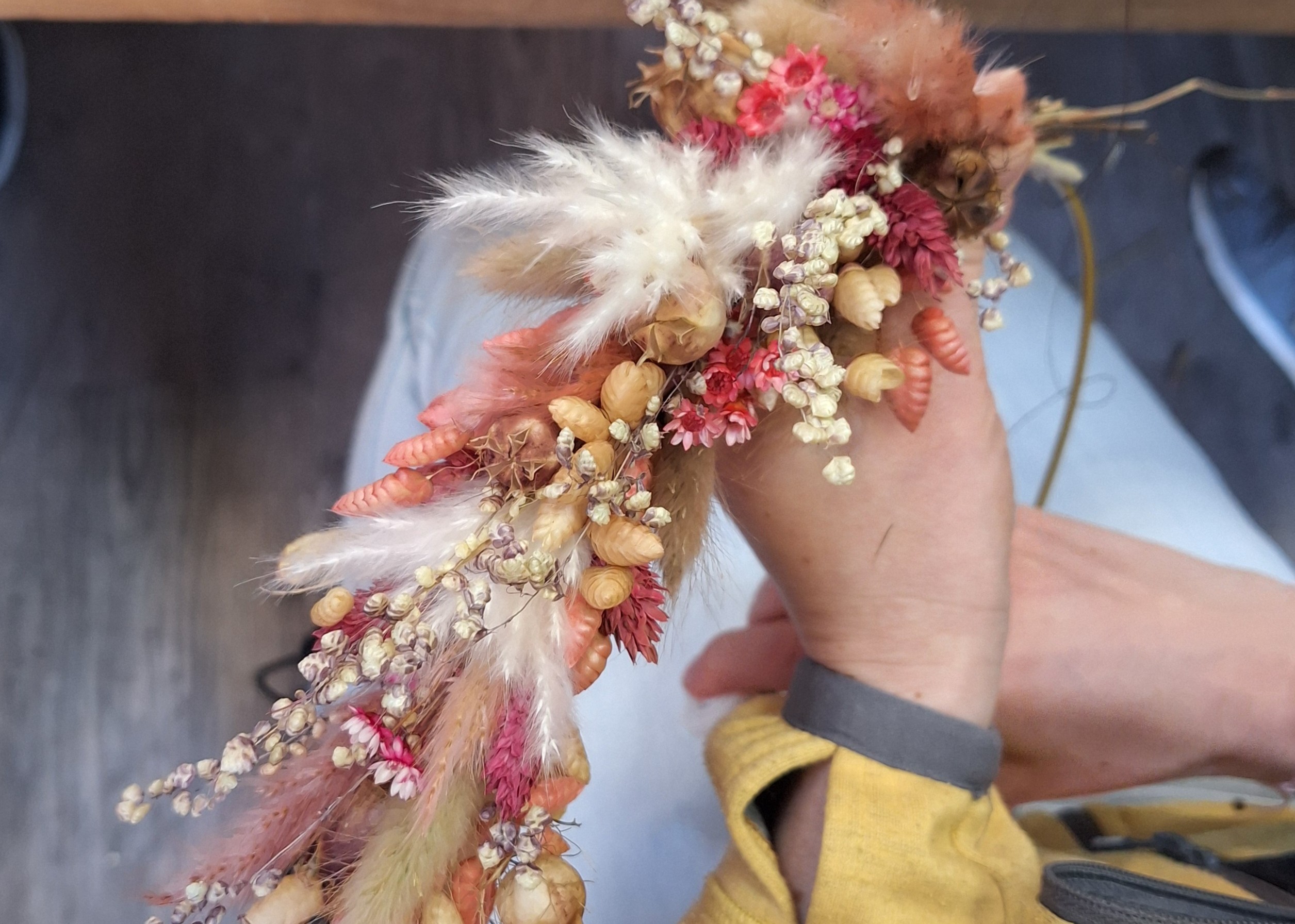 Hand hält bunten Kranz aus Trockenblumen.