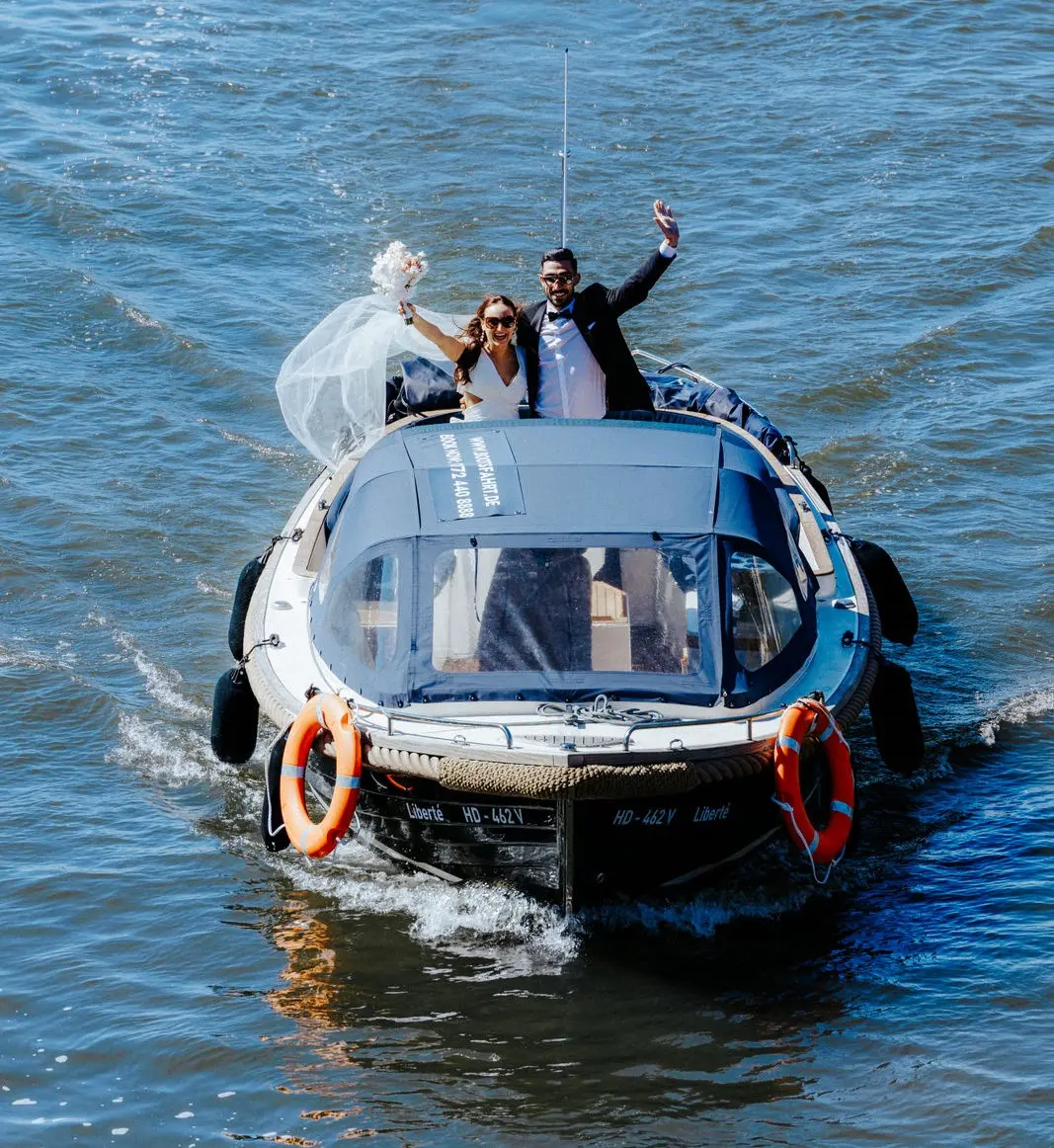 Bride and groom wave on boat in water.