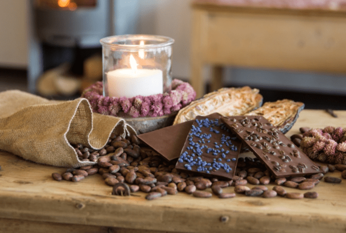 Schokoladentafeln liegen auf Kaffeebohnen, neben einer Kerze.