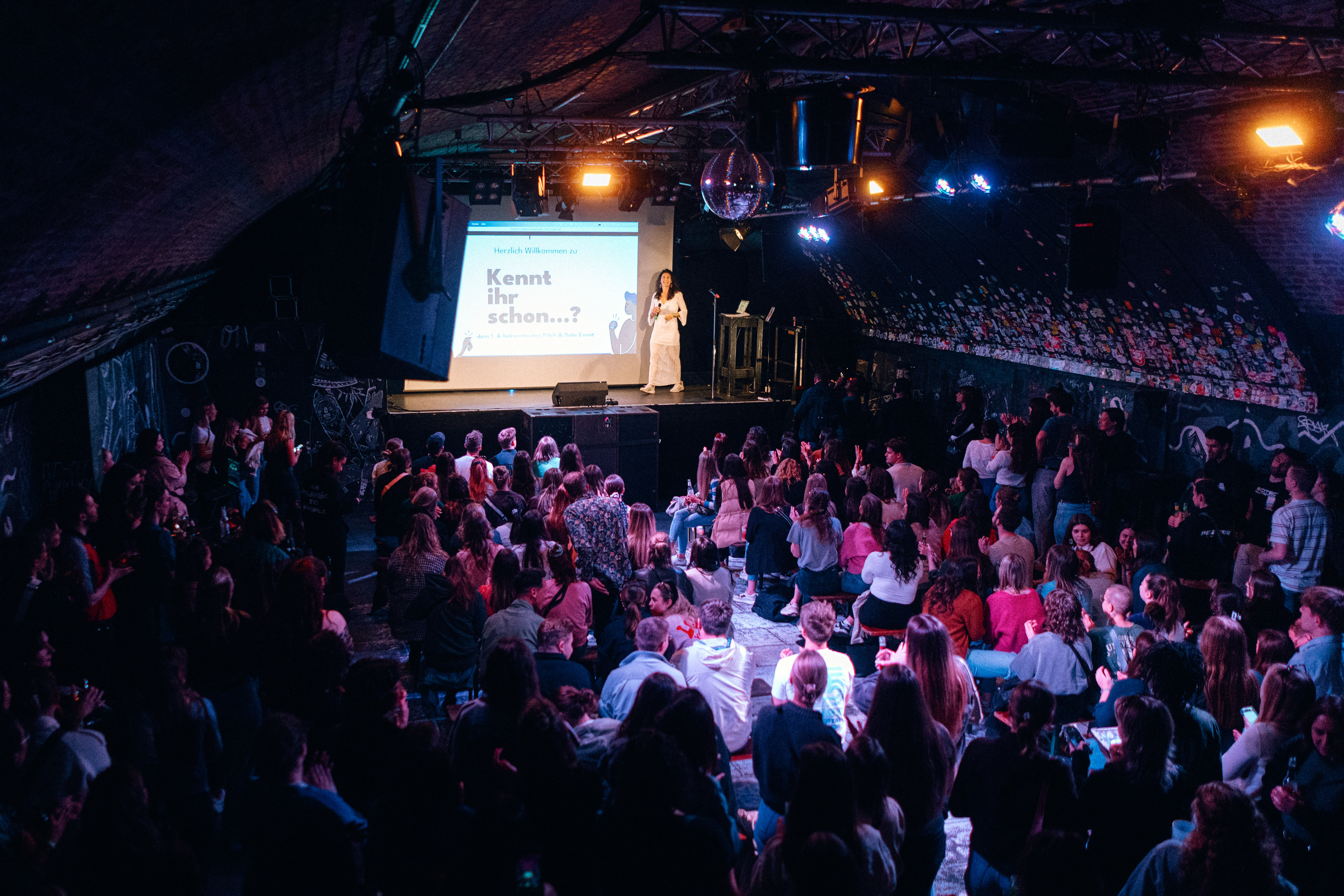 Person presenting to audience in dark venue.