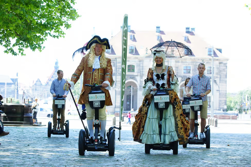 Menschen in historischen Kostümen auf Segways im Freien.